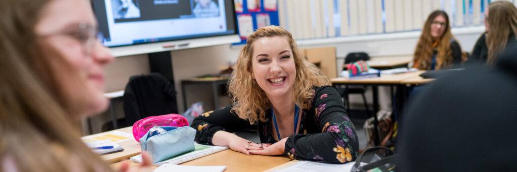 Lady smiling away from the camera, sat at a table with 2 other people who are blurred.