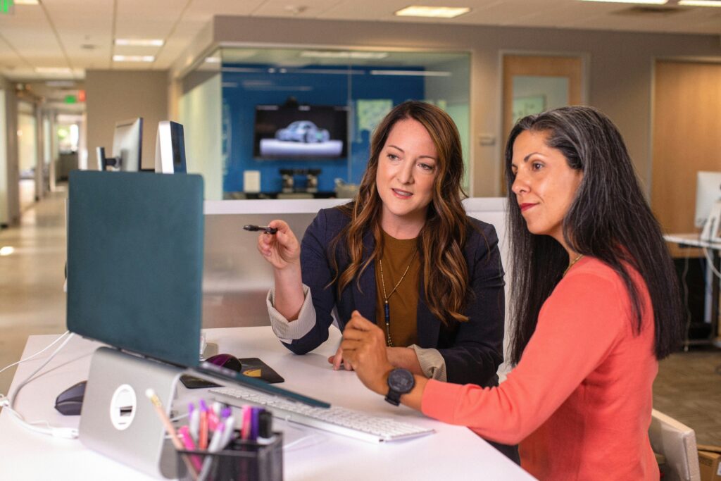 Two business women talking about sales in office at desk with laptop.